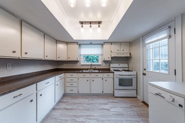 kitchen with white appliances, dark countertops, under cabinet range hood, a sink, and a tray ceiling