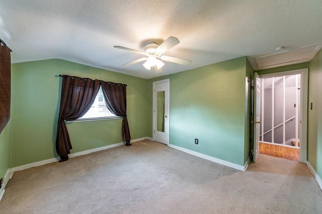 empty room featuring carpet floors, a ceiling fan, attic access, a textured ceiling, and baseboards