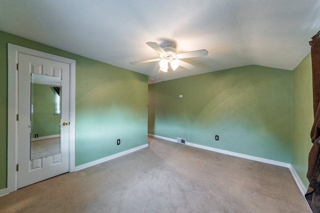 empty room featuring a textured ceiling, carpet flooring, vaulted ceiling, and ceiling fan