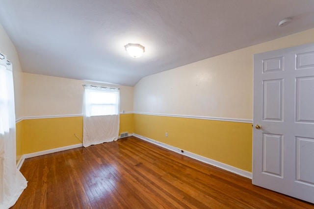 empty room with wood-type flooring, baseboards, vaulted ceiling, and visible vents