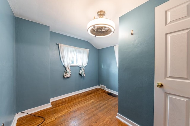 empty room with visible vents, baseboards, vaulted ceiling, and wood finished floors