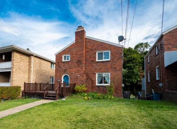 back of house with a lawn, brick siding, a chimney, and a wooden deck