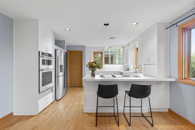 kitchen with white cabinetry, light hardwood / wood-style flooring, stainless steel appliances, and kitchen peninsula