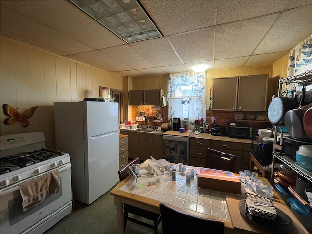 kitchen with a drop ceiling, white appliances, and tile counters