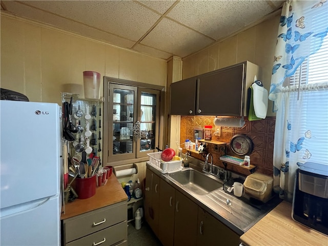 kitchen with a drop ceiling, dark brown cabinets, white refrigerator, and sink