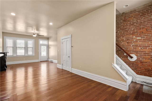 unfurnished living room featuring hardwood / wood-style floors, ceiling fan, and brick wall