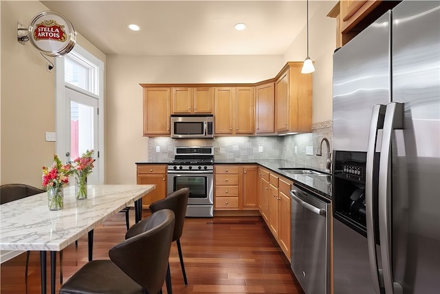 kitchen featuring pendant lighting, dark stone counters, sink, appliances with stainless steel finishes, and dark hardwood / wood-style flooring