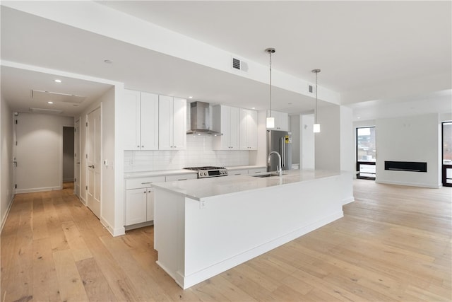 kitchen with light wood-type flooring, white cabinetry, appliances with stainless steel finishes, and wall chimney range hood