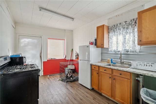 kitchen with white fridge, light wood-type flooring, crown molding, black gas range, and sink