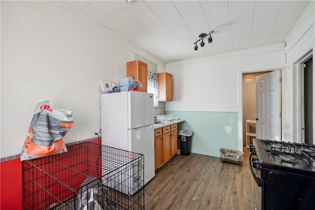 kitchen featuring light wood-type flooring, gas stove, white refrigerator, and crown molding