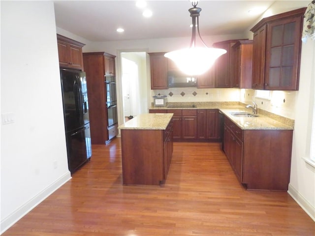 kitchen with black refrigerator, light hardwood / wood-style flooring, hanging light fixtures, and sink