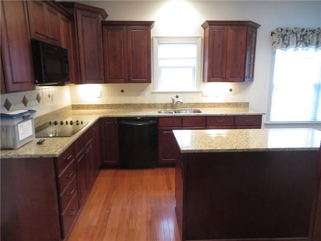 kitchen with black appliances, light stone countertops, sink, and light hardwood / wood-style flooring