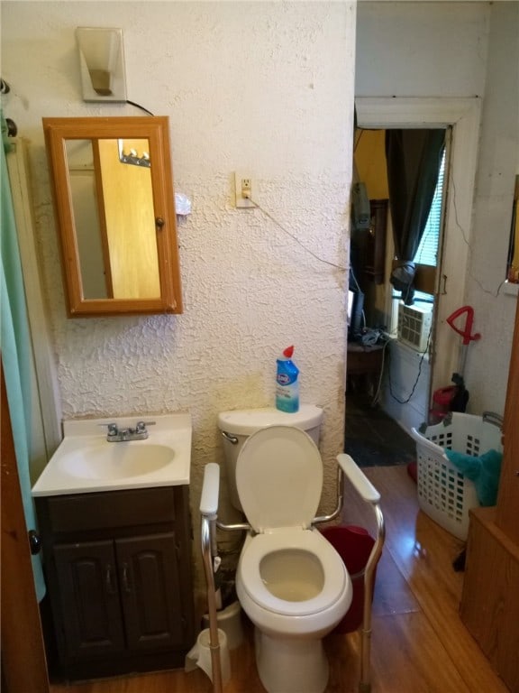 bathroom with wood-type flooring, cooling unit, vanity, and toilet