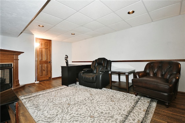 sitting room featuring a multi sided fireplace, dark hardwood / wood-style flooring, and a drop ceiling