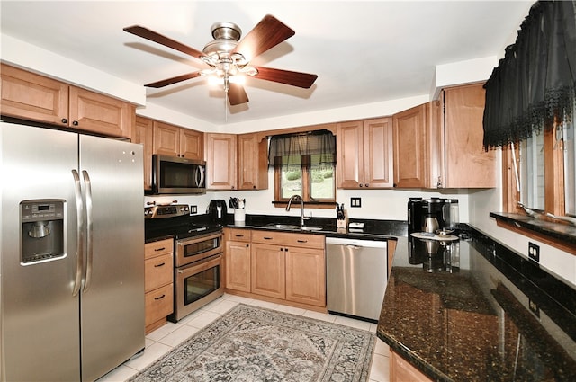 kitchen with dark stone countertops, light tile patterned flooring, stainless steel appliances, ceiling fan, and sink