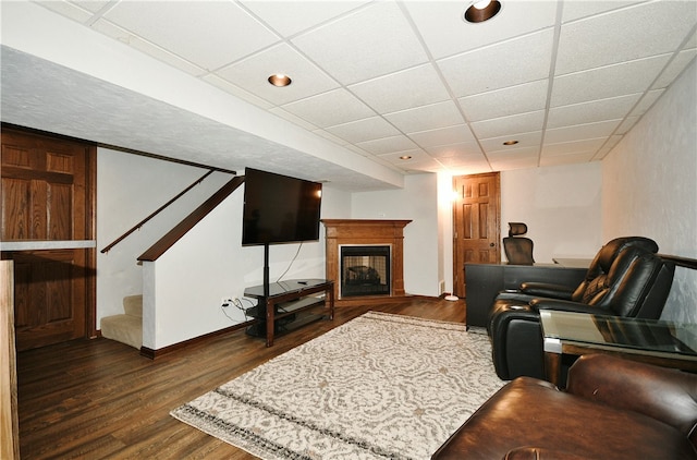 living room featuring a multi sided fireplace, a drop ceiling, and dark wood-type flooring