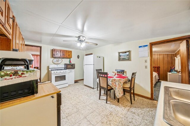 kitchen with white appliances, wood walls, sink, and ceiling fan