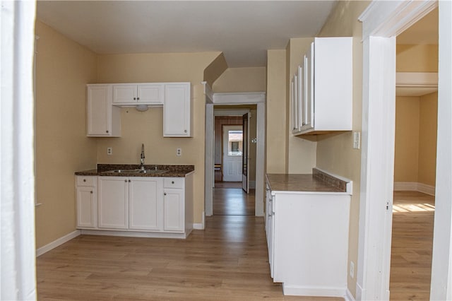 kitchen with dark stone counters, light wood-type flooring, white cabinets, and sink