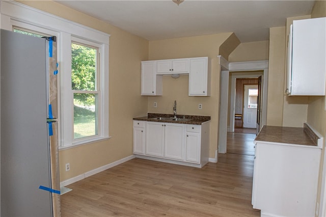 kitchen featuring white cabinets, stainless steel refrigerator, light wood-type flooring, and sink