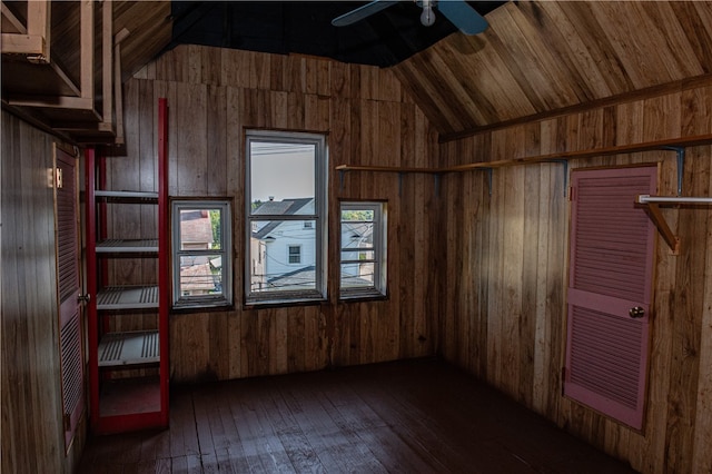 empty room featuring wooden walls, vaulted ceiling, plenty of natural light, and dark wood-type flooring