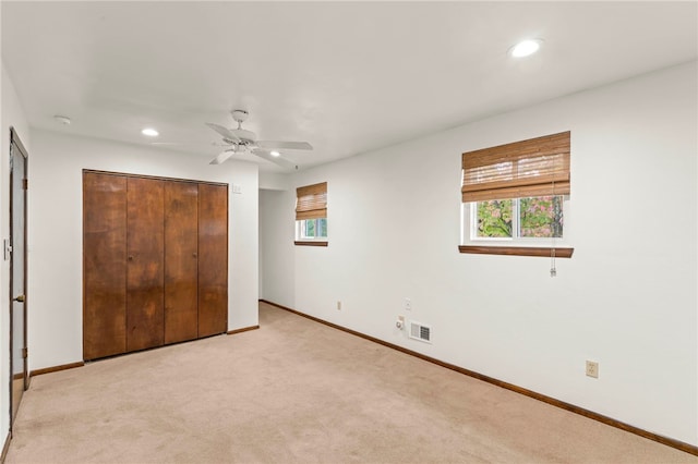 unfurnished bedroom featuring ceiling fan, light colored carpet, and a closet