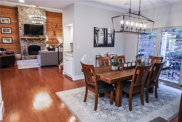 dining area with a fireplace, wooden walls, a notable chandelier, and dark wood-type flooring