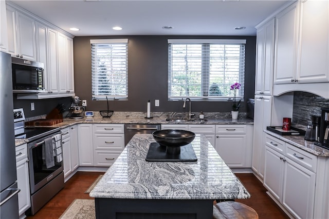 kitchen with light stone counters, sink, appliances with stainless steel finishes, a center island, and white cabinetry