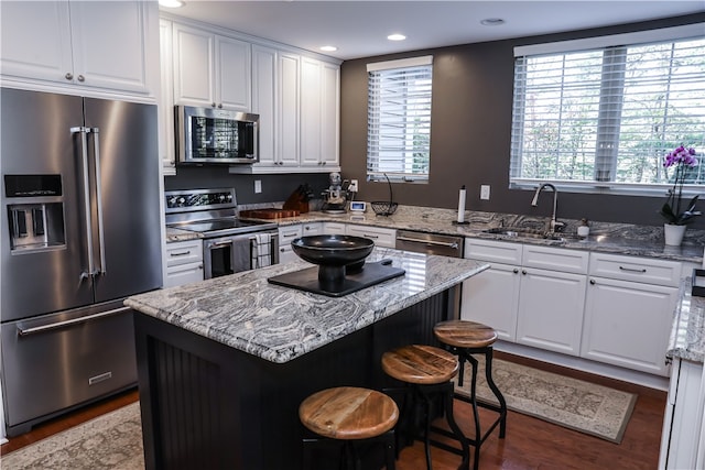 kitchen with sink, white cabinetry, appliances with stainless steel finishes, a center island, and light stone countertops