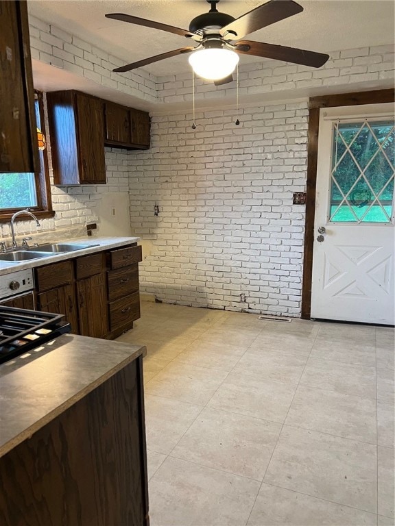 kitchen with brick wall, dark brown cabinetry, sink, and ceiling fan