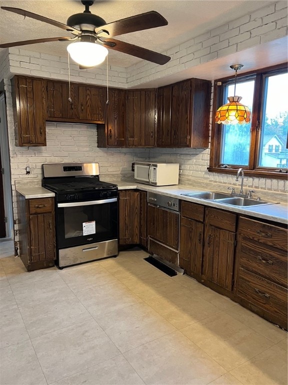 kitchen featuring dark brown cabinetry, ceiling fan, sink, stainless steel range with gas stovetop, and decorative light fixtures