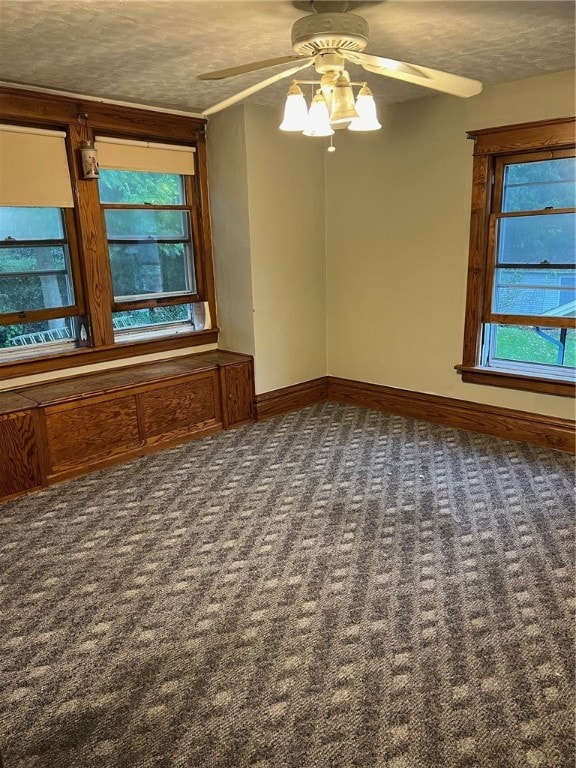 spare room with a textured ceiling, dark colored carpet, and a healthy amount of sunlight