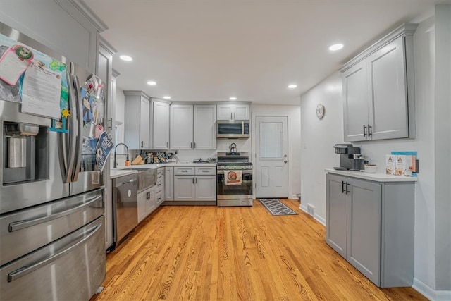 kitchen with gray cabinetry, stainless steel appliances, light wood-type flooring, and sink