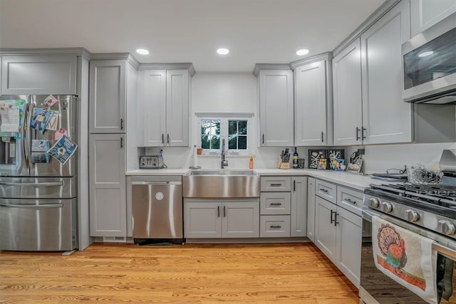 kitchen with appliances with stainless steel finishes, gray cabinetry, sink, and light hardwood / wood-style flooring