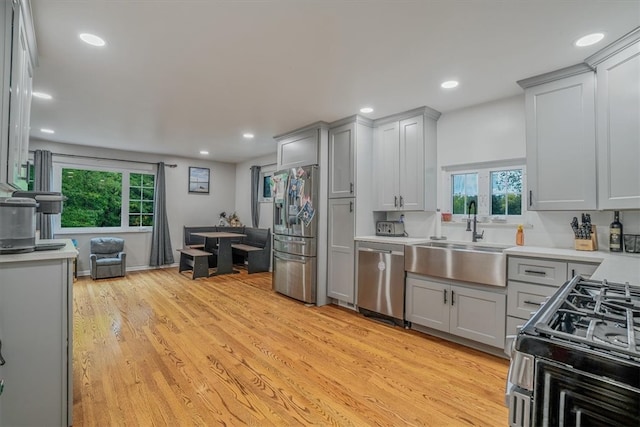 kitchen with appliances with stainless steel finishes, light wood-type flooring, sink, and gray cabinets