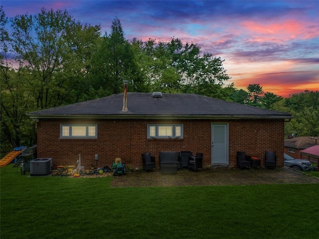 back house at dusk with a lawn and cooling unit