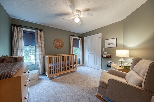 carpeted bedroom featuring a closet, ceiling fan, a crib, and a textured ceiling