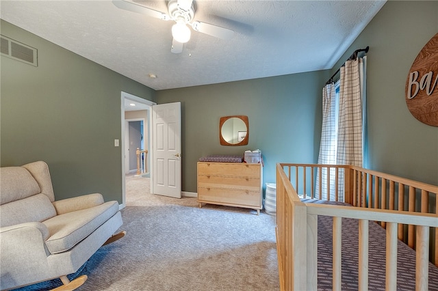 bedroom featuring ceiling fan, a nursery area, a textured ceiling, and light carpet