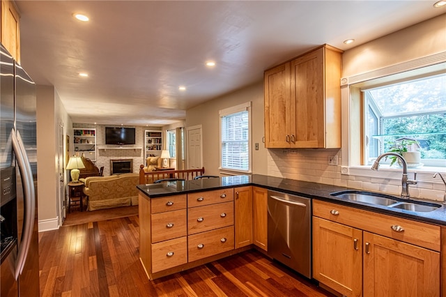 kitchen featuring sink, kitchen peninsula, dark wood-type flooring, stainless steel appliances, and a fireplace