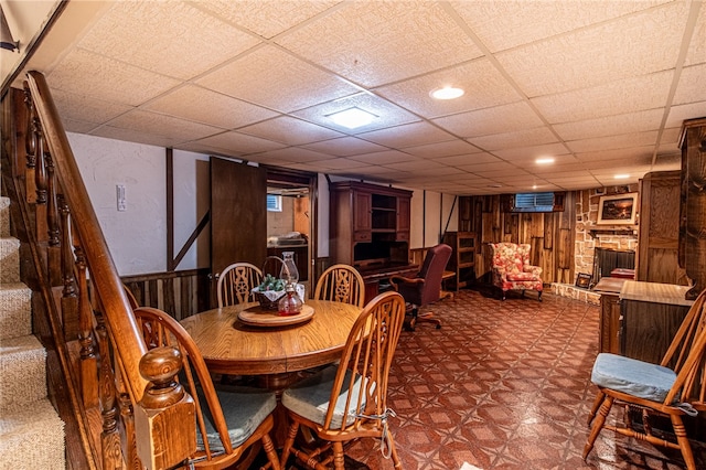 dining area with a stone fireplace, wooden walls, and a paneled ceiling