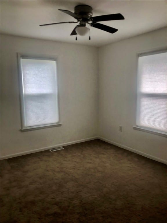 spare room with ceiling fan, dark carpet, and plenty of natural light