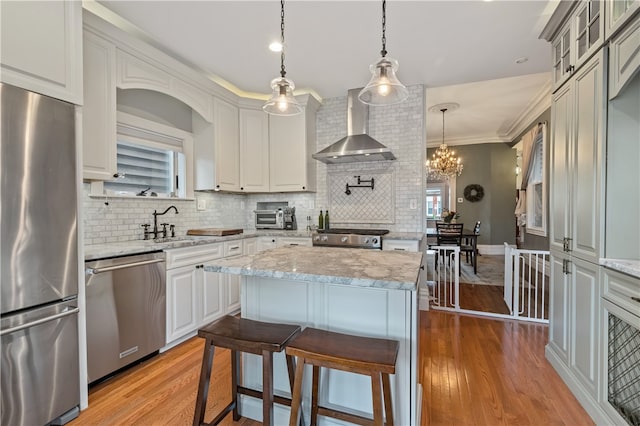 kitchen featuring crown molding, light wood-type flooring, appliances with stainless steel finishes, a breakfast bar, and wall chimney exhaust hood