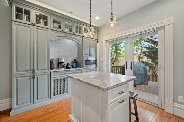 kitchen with tasteful backsplash, light wood-type flooring, light stone countertops, stainless steel microwave, and a center island