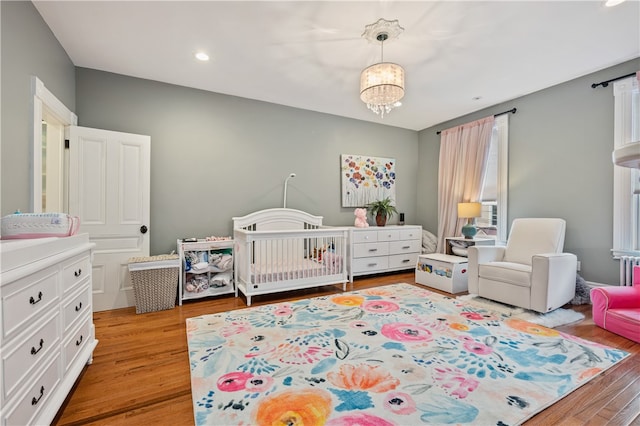 bedroom with a crib, a chandelier, and light wood-type flooring