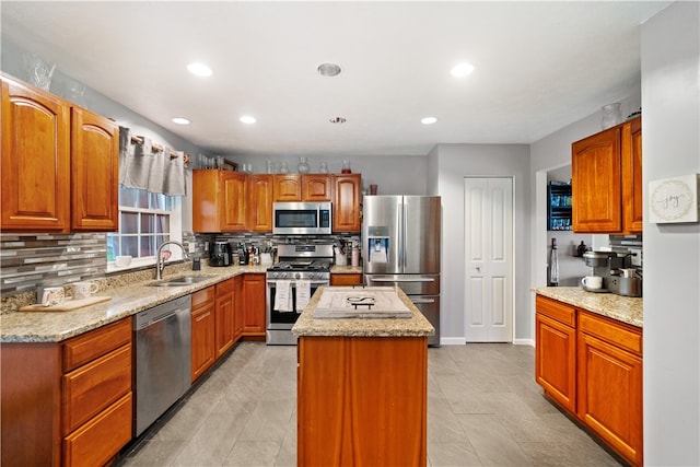 kitchen with light stone counters, backsplash, a kitchen island, stainless steel appliances, and sink