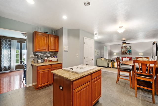 kitchen featuring ceiling fan, white electric stovetop, a center island, light stone countertops, and decorative backsplash