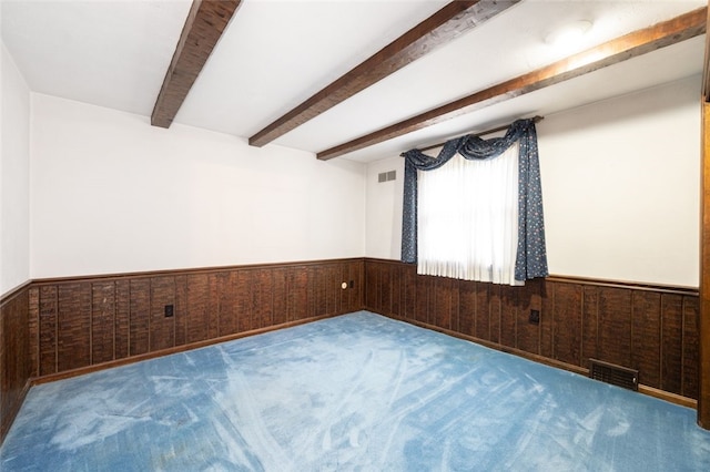 spare room featuring beam ceiling, carpet flooring, and wood walls