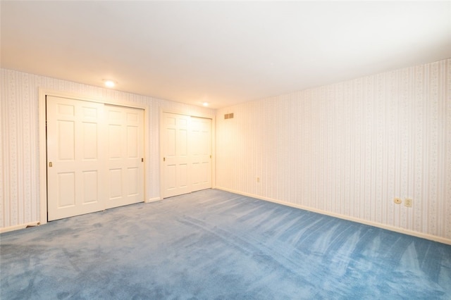 unfurnished bedroom with dark colored carpet and multiple closets