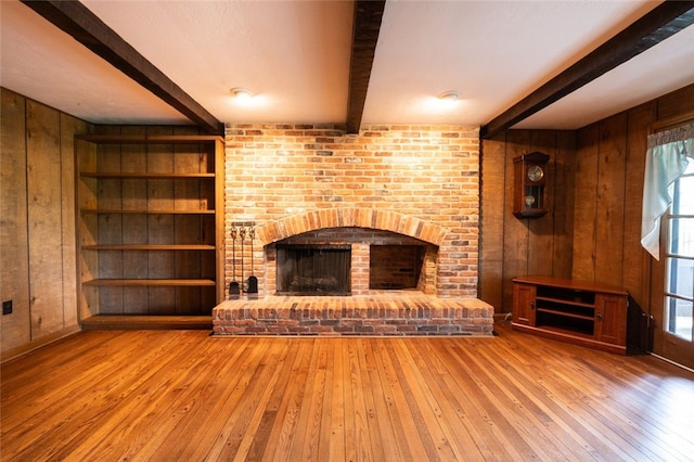 unfurnished living room with a brick fireplace, hardwood / wood-style flooring, wood walls, and a wealth of natural light