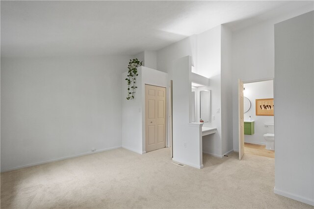 unfurnished bedroom featuring connected bathroom, a towering ceiling, and light colored carpet