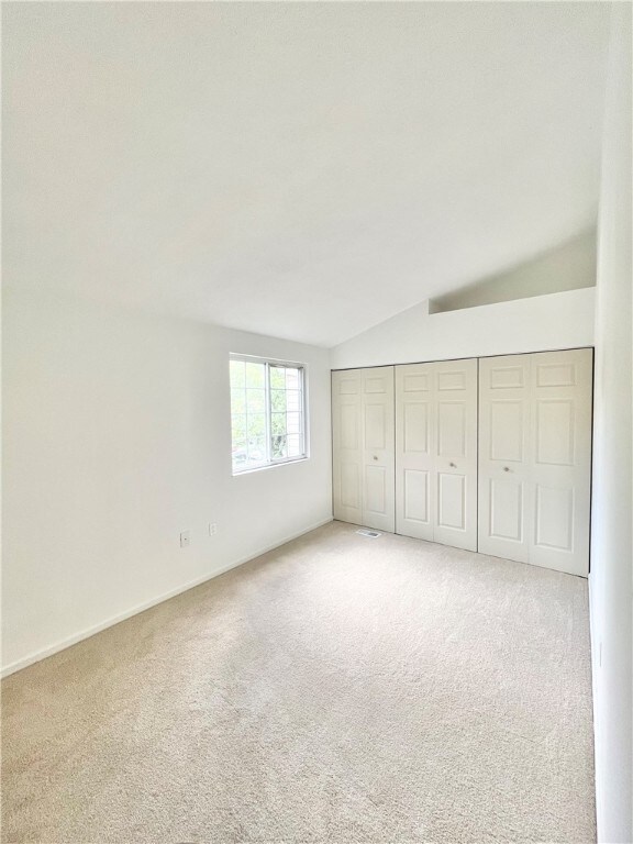 unfurnished bedroom with vaulted ceiling, a closet, and light colored carpet